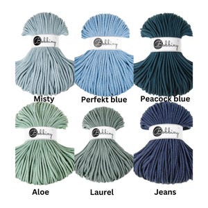 May include: Six skeins of Bobbiny cord arranged in two rows. The top row features Misty, Perfekt blue, and Peacock blue. The bottom row displays Aloe, Laurel, and Jeans. Each skein is secured with a white paper band labeled with the brand name.