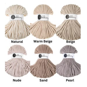 May include: Six skeins of Bobbiny cotton cord arranged in two rows. Each skein is secured with a white paper band featuring the Bobbiny logo. The colors displayed are labeled as Natural, Warm Beige, Beige, Nude, Sand, and Pearl, showing various neutral shades of off-white, tan, brown, and light gray.
