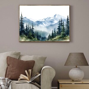 May include: A rectangular wall art print featuring a watercolour landscape of snow-capped mountains and a dense forest of dark green and blue pine trees. The scene depicts a misty valley with layered peaks in the background and tall evergreen trees.