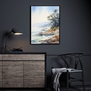 May include: Watercolor painting of a coastal landscape with a black frame. The artwork depicts a rocky shoreline, ocean waves, and evergreen trees under a soft blue sky. The painting is displayed on a dark gray wall above a wooden cabinet.