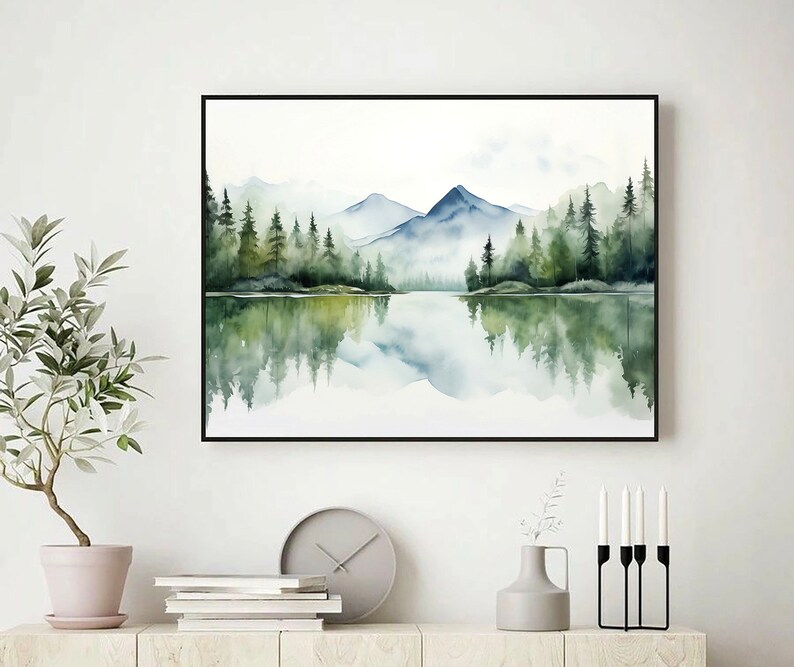 May include: A watercolor painting of a mountain lake scene with a reflection of the trees and mountains in the water. The painting is framed in a black frame.