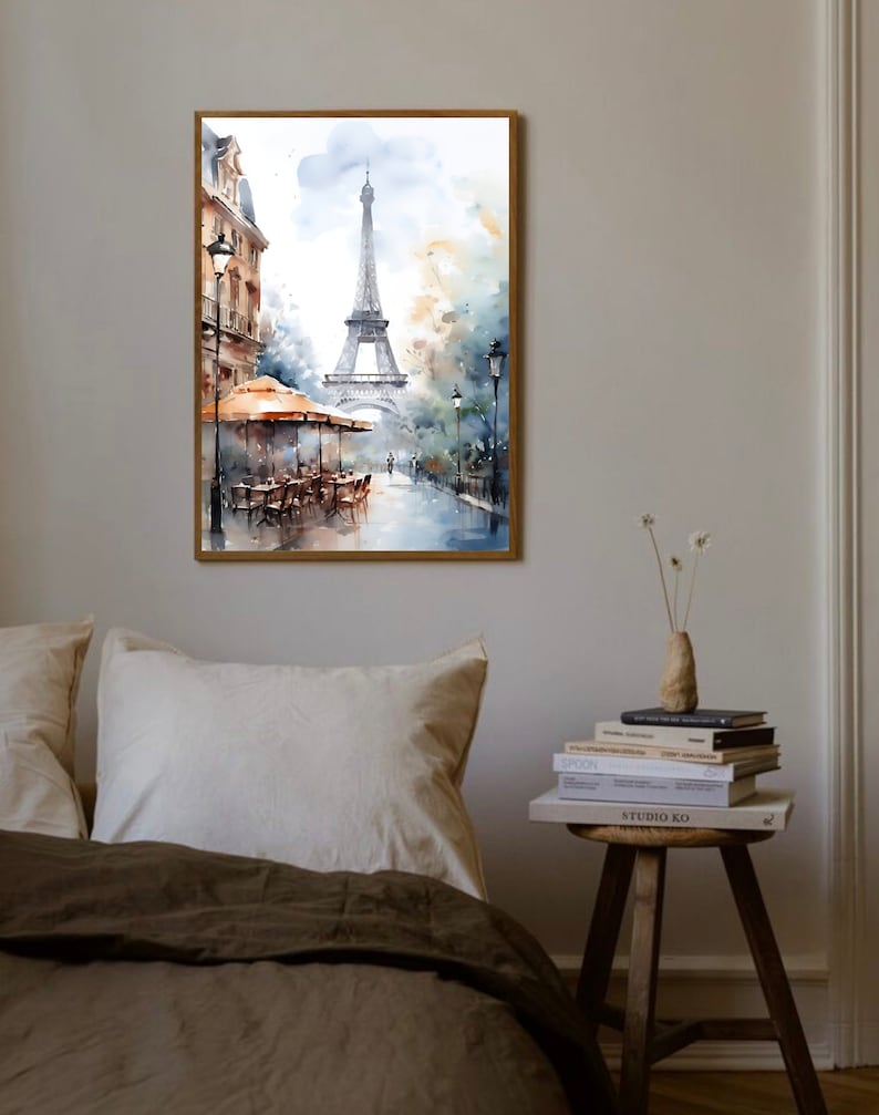 K&ouml;nnte beinhalten: Ein Aquarellbild des Eiffelturms in Paris, Frankreich. Das Bild zeigt eine Stra&szlig;enszene mit einem Caf&eacute; und Passanten. Das Bild ist in einem Holzrahmen gerahmt.