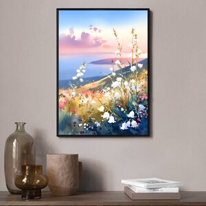 Pode incluir: Uma impress&atilde;o em aquarela emoldurada de uma paisagem. A obra de arte retrata uma colina com flores brancas em forma de sino, flores silvestres coloridas e uma vista do mar sob um c&eacute;u rosa e azul. A impress&atilde;o &eacute; exibida em uma superf&iacute;cie de madeira.