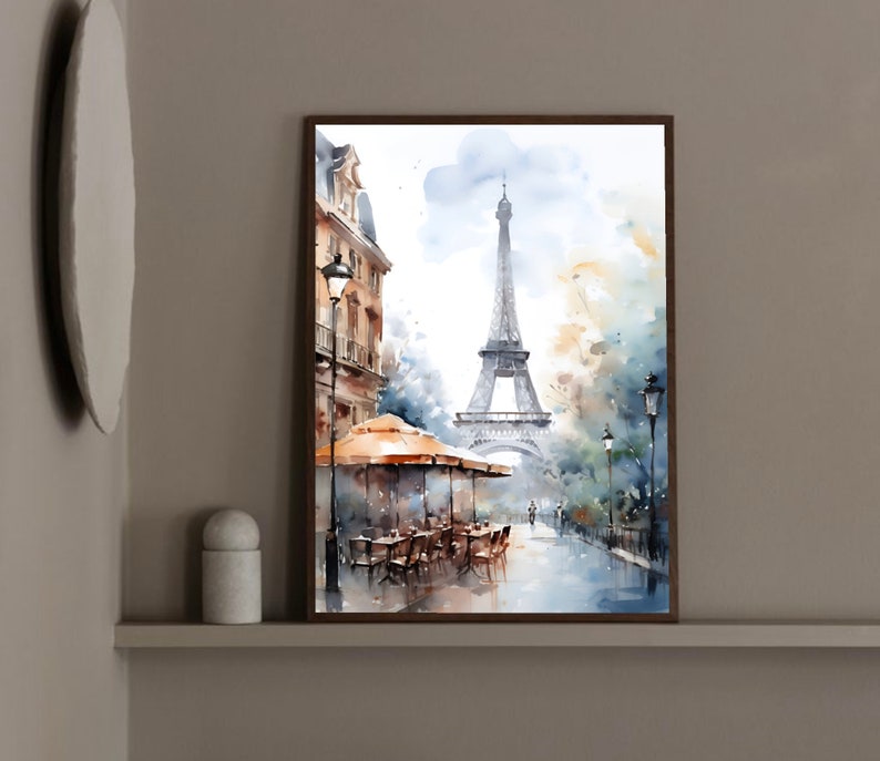 K&ouml;nnte beinhalten: Ein Aquarellgem&auml;lde einer Pariser Stra&szlig;enszene mit dem Eiffelturm im Hintergrund. Das Gem&auml;lde zeigt ein Caf&eacute; mit Tischen und St&uuml;hlen, eine Stra&szlig;enlaterne und B&auml;ume. Der Himmel ist hellblau mit wei&szlig;en Wolken.