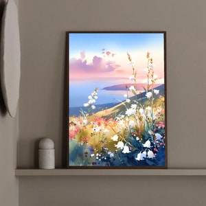 Pode incluir: Uma pintura em aquarela emoldurada retrata uma paisagem serena. Flores brancas em forma de sino florescem em primeiro plano, com uma colina e um corpo de &aacute;gua ao fundo. O c&eacute;u transita do azul para o rosa, sugerindo um p&ocirc;r do sol.