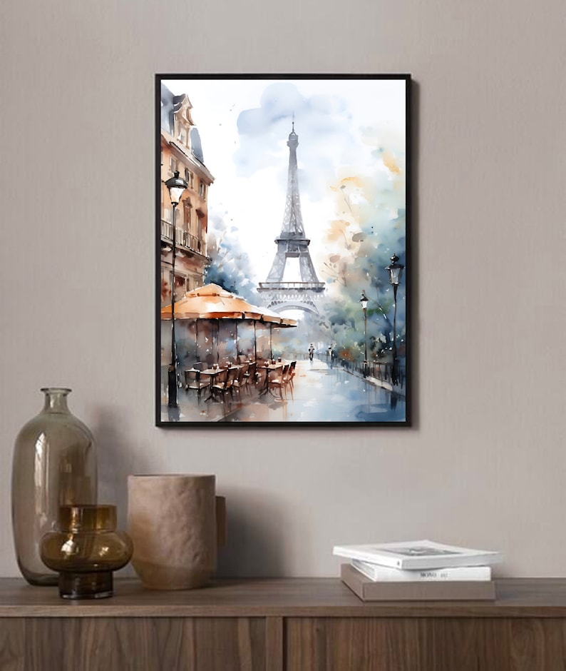 K&ouml;nnte beinhalten: Ein Aquarellbild des Eiffelturms in Paris, Frankreich. Das Bild zeigt eine Stra&szlig;enszene mit einem Caf&eacute; und Passanten. Der Turm befindet sich im Hintergrund, das Caf&eacute; im Vordergrund. Das Bild ist in einer weichen, ged&auml;mpften Farbpalette gehalten.
