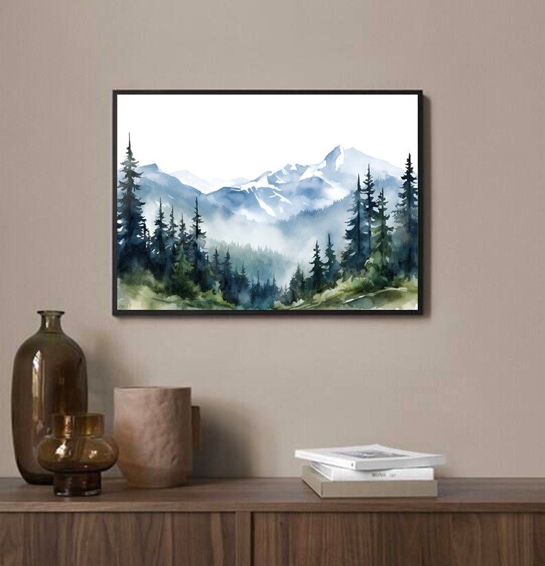 May include: A rectangular wall art print in a black frame featuring a watercolour landscape painting of snow-capped mountains rising above a dense forest of dark green and blue pine trees with soft mist settling between the trees and peaks.