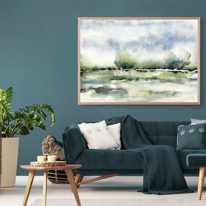 Op de afbeelding: Een tealblauwe woonkamer met een donkerblauwe fluwelen bank, een houten salontafel, een plant in een pot en een ingelijst aquarel schilderij van een landschap met bomen en water.