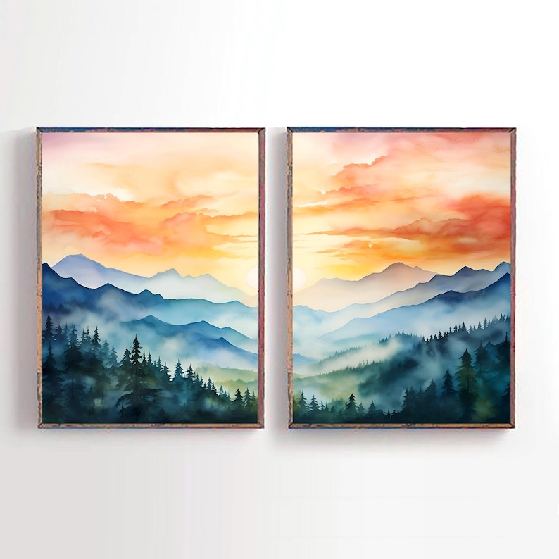 May include: Two framed watercolor landscape paintings. Each features a mountain range with a forest in the foreground. The sky is a blend of orange and yellow hues, with blue and green tones in the mountains.