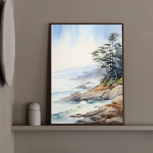 May include: Watercolor painting of a coastal landscape with a rocky shoreline, ocean waves, and evergreen trees. The artwork is framed in a dark brown wooden frame. The sky is a soft blue, and the overall color palette is muted.
