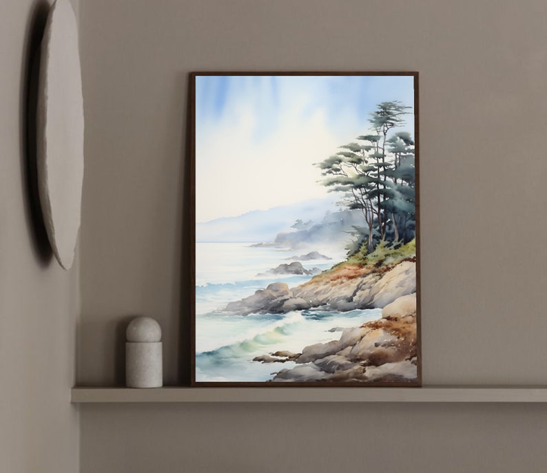 May include: Watercolor painting of a coastal landscape with a rocky shoreline, ocean waves, and evergreen trees. The artwork is framed in a dark brown wooden frame. The sky is a soft blue, and the overall color palette is muted.