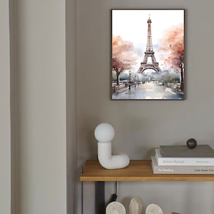 May include: A watercolor painting of the Eiffel Tower in Paris, France. The painting is framed and hanging on a light gray wall. There is a white ceramic lamp on a wooden shelf below the painting.