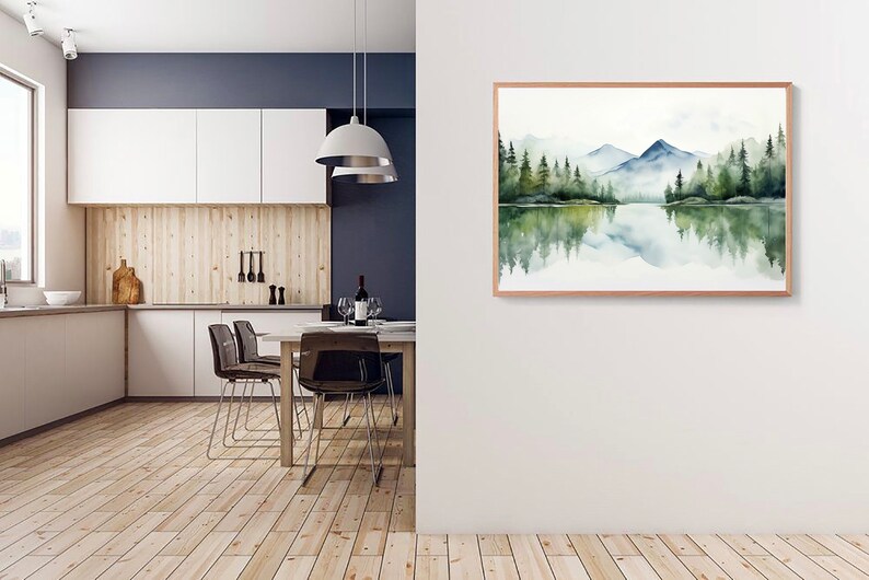 May include: A watercolor painting of a mountain lake scene with a reflection of the mountains and trees in the water. The painting is framed in a light wood frame and is hanging on a white wall.