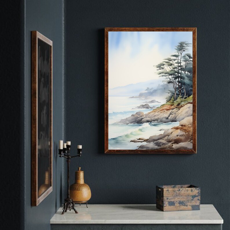 May include: Watercolor painting of a coastal landscape with a rocky shoreline, ocean waves, and trees. The artwork is framed in a dark wood frame. The painting is displayed on a dark blue wall, with a decorative candle holder and a wooden box on a white surface.