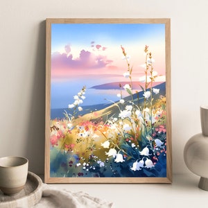Pode incluir: Uma impress&atilde;o em aquarela emoldurada de uma paisagem costeira com flores silvestres brancas em primeiro plano. A obra apresenta uma paleta de cores suaves de azuis, rosas e amarelos, com uma vista do mar e do c&eacute;u.