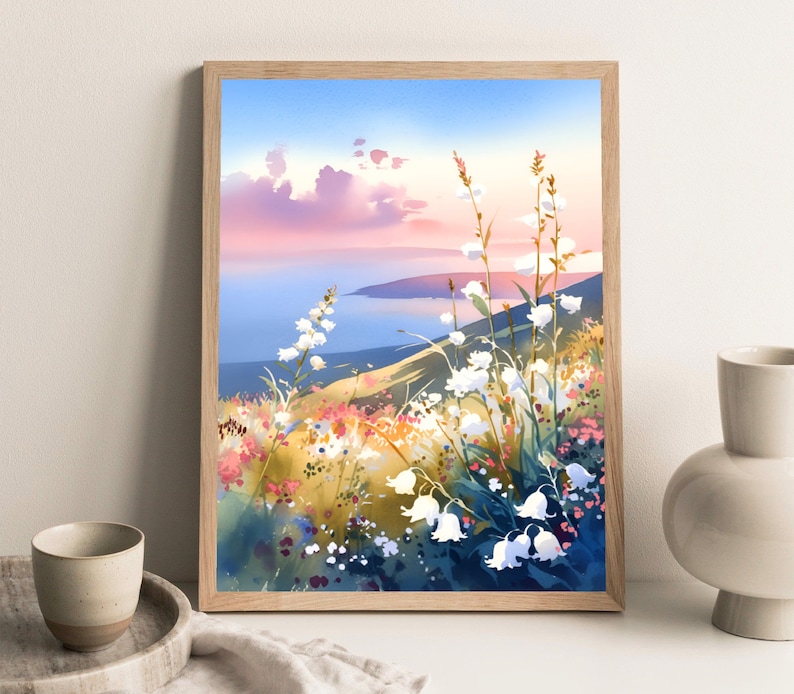 Pode incluir: Uma impress&atilde;o em aquarela emoldurada de uma paisagem costeira com flores silvestres brancas em primeiro plano. A obra apresenta uma paleta de cores suaves de azuis, rosas e amarelos, com uma vista do mar e do c&eacute;u.