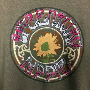 May include: A green t-shirt with a circular graphic design. The graphic features a sunflower with a brown, green, and yellow color scheme. The text "21st Century Hippie" is written in a stylized font around the sunflower.