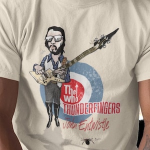 May include: A beige t-shirt with a cartoon illustration of John Entwistle from The Who playing a bass guitar. The text "The Who's Thunderfingers John Entwistle" is printed on the shirt.