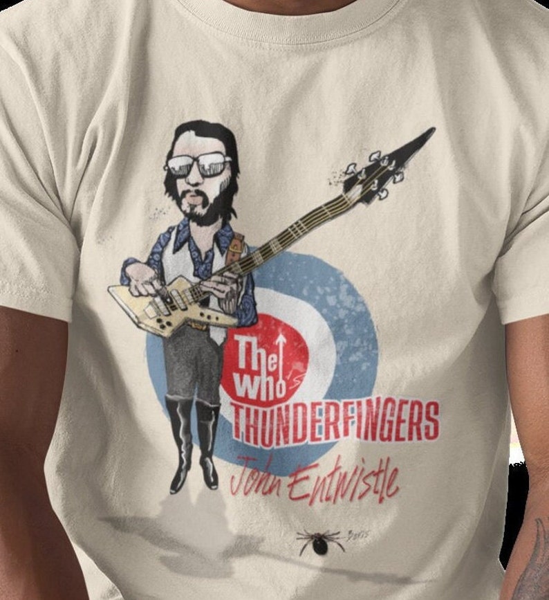 May include: A beige t-shirt with a cartoon illustration of John Entwistle from The Who playing a bass guitar. The text "The Who's Thunderfingers John Entwistle" is printed on the shirt.