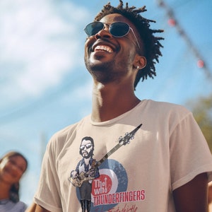 May include: A man wearing a white t-shirt with a cartoon illustration of John Entwistle from The Who playing a bass guitar. The shirt has the text "The Who Thunderfingers John Entwistle" printed on it.