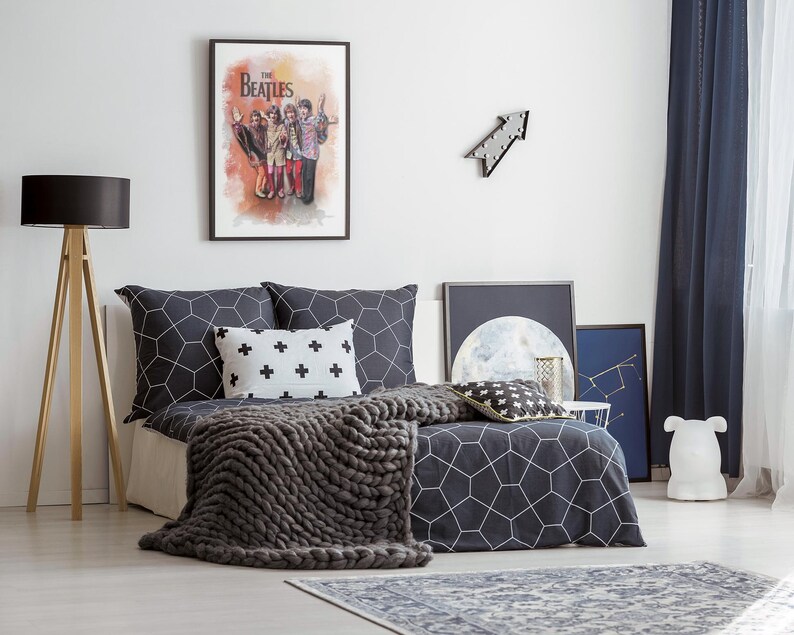 K&ouml;nnte beinhalten: Ein Schlafzimmer mit einem Bett, das mit dunkelgrauer Bettw&auml;sche mit wei&szlig;em geometrischem Muster, einem wei&szlig;en Kissen mit schwarzen Pluszeichen und einer grob gestrickten grauen Decke ausgestattet ist. Ein gerahmtes Beatles-Poster h&auml;ngt an der Wand.