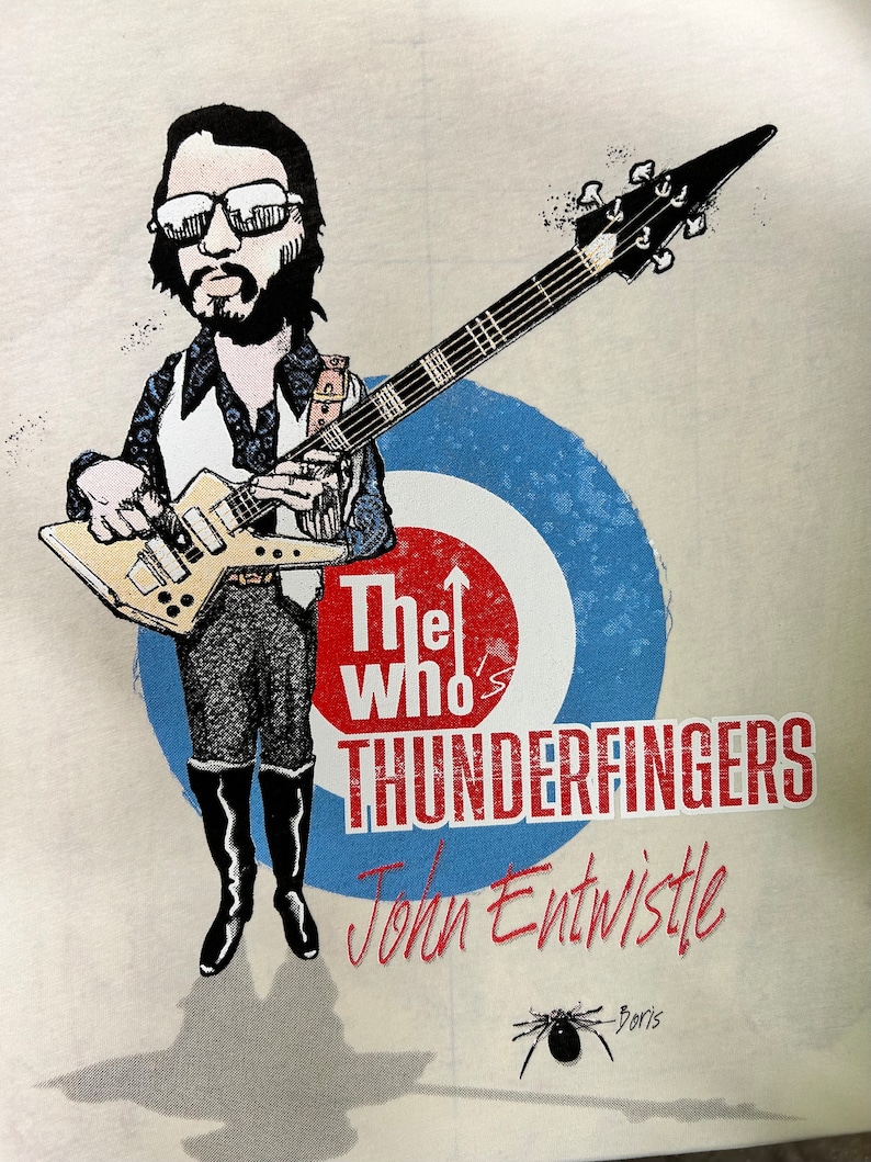 May include: A cartoon illustration of John Entwistle, bassist for The Who, playing a guitar. The image includes the band's name, "The Who's Thunderfingers", and Entwistle's signature. The background features a blue and white target.