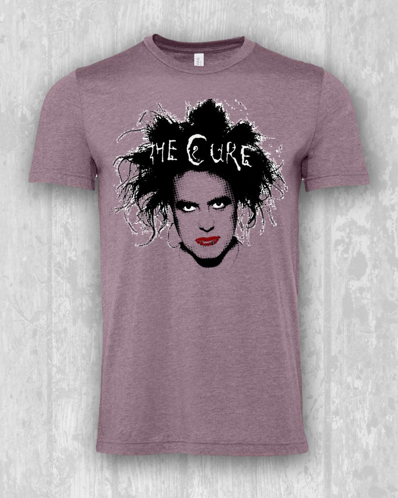 May include: A heather purple t-shirt with a black and white graphic of Robert Smith, the lead singer of The Cure, with the band's name printed above his head.