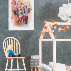 K&ouml;nnte beinhalten: Ein gerahmter Wandkunstdruck mit einer Illustration im Aquarellstil der Band The Beatles. Die vier Mitglieder sind zusammenstehend in farbenfroher, gemusterter Kleidung vor einem weichen, orange und gelb verlaufenden Hintergrund dargestellt.