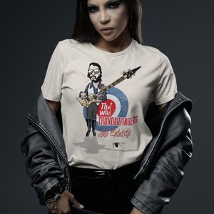 May include: A woman wearing a white t-shirt with a graphic of John Entwistle from The Who, playing a guitar. The graphic includes the text "The Who Thunderfingers John Entwistle".
