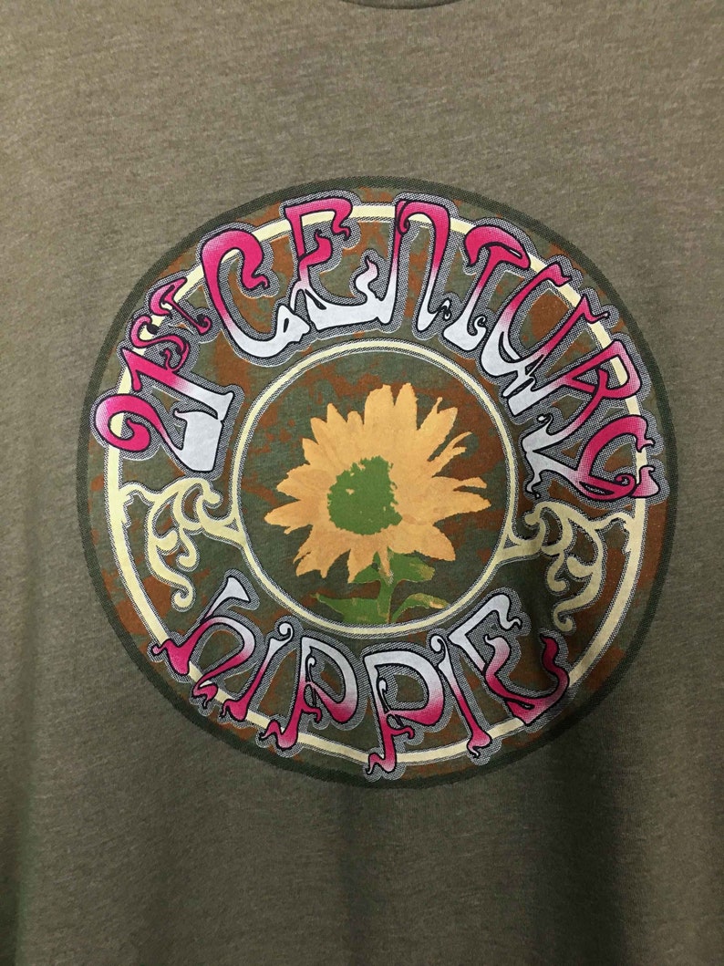 May include: A green t-shirt with a circular graphic design. The graphic features a sunflower with a brown, green, and yellow color scheme. The text "21st Century Hippie" is written in a stylized font around the sunflower.