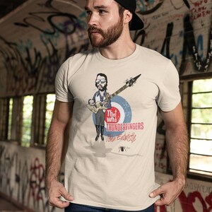 May include: A white t-shirt with a cartoon illustration of John Entwistle from The Who playing a bass guitar. The text "The Who Thunderfingers John Entwistle" is printed on the shirt.