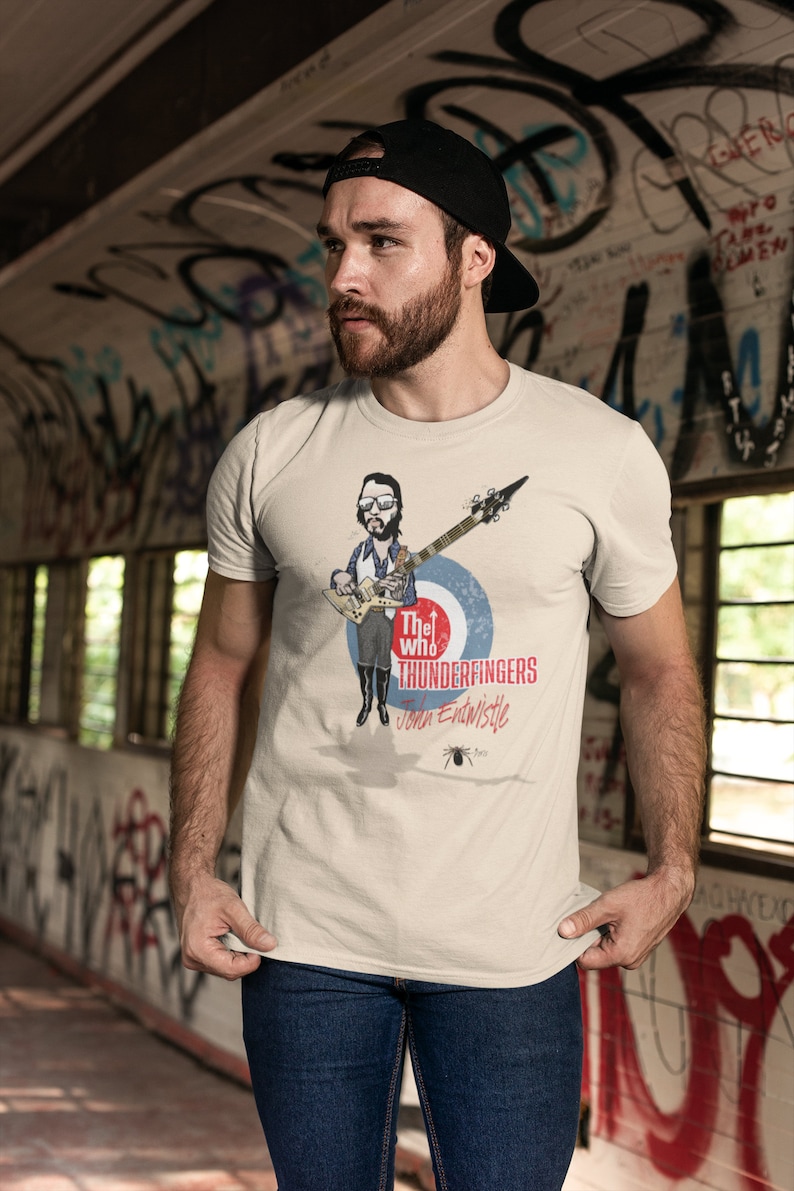 May include: A white t-shirt with a cartoon illustration of John Entwistle from The Who playing a bass guitar. The text "The Who Thunderfingers John Entwistle" is printed on the shirt.