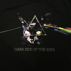 May include: Black t-shirt with a graphic of a black cat's face in a triangle with a rainbow prism beam of light. The text "DARK SIDE OF THE SOFA" is printed below the graphic.