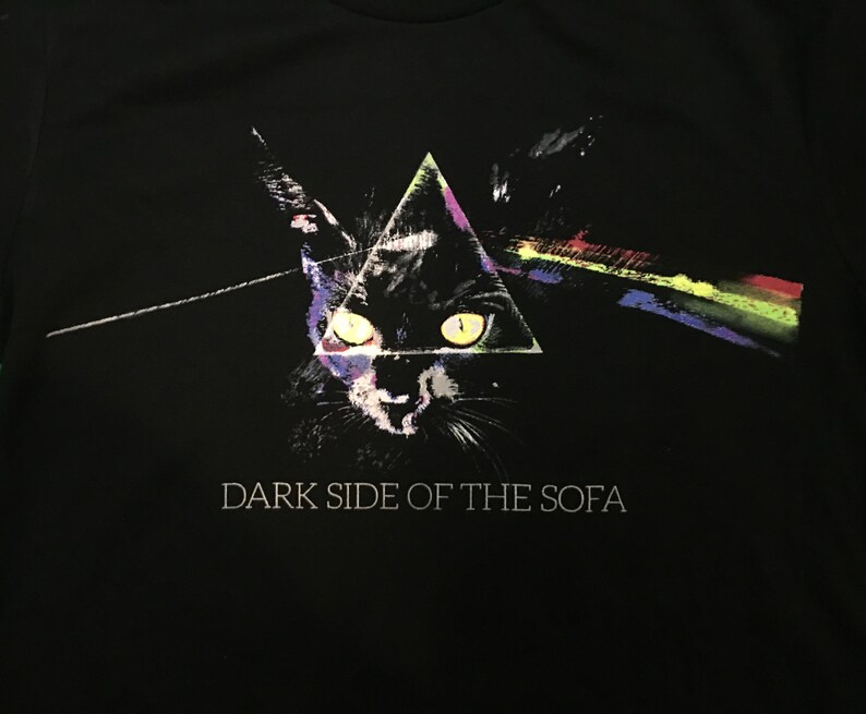 May include: Black t-shirt with a graphic of a black cat's face in a triangle with a rainbow prism beam of light. The text "DARK SIDE OF THE SOFA" is printed below the graphic.