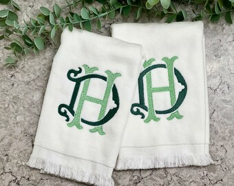 May include: Two white hand towels with a green and dark green embroidered monogram. The towels have a fringe along the bottom edge. The monogram features the letters "DH" in a decorative font.