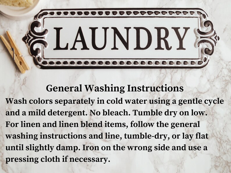 May include: A white and black laundry sign with the word "LAUNDRY". The sign has decorative edges and includes general washing instructions. A wooden clothes peg is visible. The sign is on a marble surface.