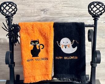 May include: Two Halloween themed kitchen towels. One towel is orange with a black cat and the text "Happy Halloween". The other towel is black with a white ghost holding a "BOO" banner and the text "Happy Halloween".