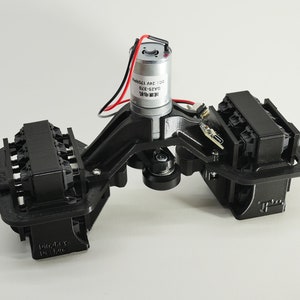 以下が含まれることがあります： 銀色のモーターと配線が付いた黒色の機械部品。この部品は、中央構造の両側に2つの長方形のセクションがあります。モーターにはテキストが印刷されています。