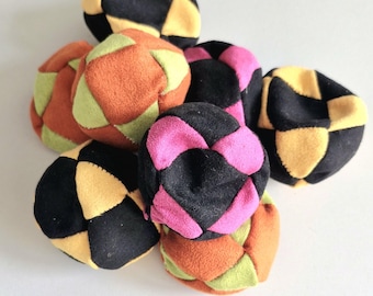 Könnte beinhalten: Eine Sammlung bunter, handgefertigter Jonglierbälle. Jeder Ball hat ein Patchwork-Design mit schwarzen, gelben, orangefarbenen, grünen und rosa Segmenten. Die Bälle sind in einem Haufen angeordnet und zeigen ihre lebendigen Farben und Texturen.