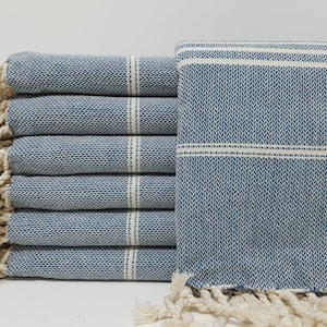May include: A stack of six blue and white striped towels with white fringe. The towels are folded and stacked on a white surface.