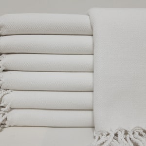 May include: A stack of white towels with fringed edges. The towels are folded neatly and have a soft, textured surface.