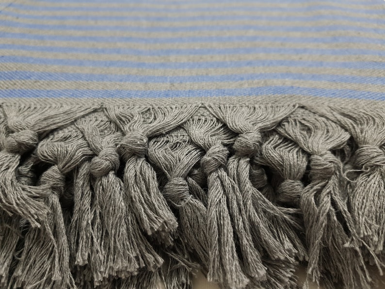 May include: Gray and blue striped throw blanket with fringe tassels. The blanket is made of a soft, woven fabric.