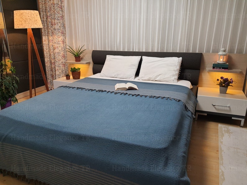 May include: A blue bedspread with white stripes and tassels, on a bed with white pillows and a headboard. There are two nightstands with lamps and a book on the bed.