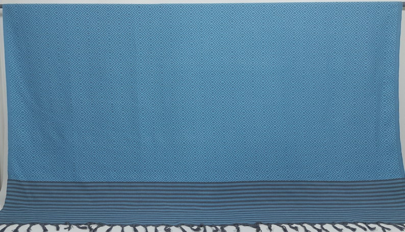 May include: A blue and gray patterned Turkish towel with fringe. The towel has a geometric pattern and a solid blue border.