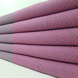 Puede incluir: Pila de toallas de color rosa y gris con un diseño de chevron. Las toallas están dobladas y apiladas unas sobre otras.