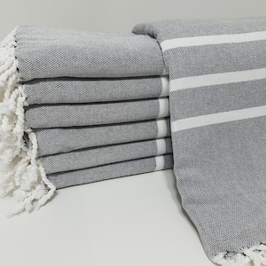 May include: A stack of gray and white striped towels with white fringe. The towels are folded and stacked on a white surface.