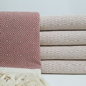 May include: A stack of red and white patterned Turkish towels with fringe. The towels are made of cotton and are soft and absorbent.
