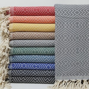 May include: Ten different patterned Turkish towels, stacked on top of each other. The towels are all different colors, including red, orange, yellow, brown, gray, green, blue, and black. The towels have a fringe on the bottom.