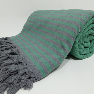 May include: A gray and green striped Turkish towel with fringe. The towel is rolled up and has a soft, textured feel.