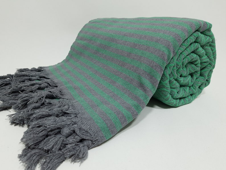 May include: A gray and green striped Turkish towel with fringe. The towel is rolled up and has a soft, textured feel.